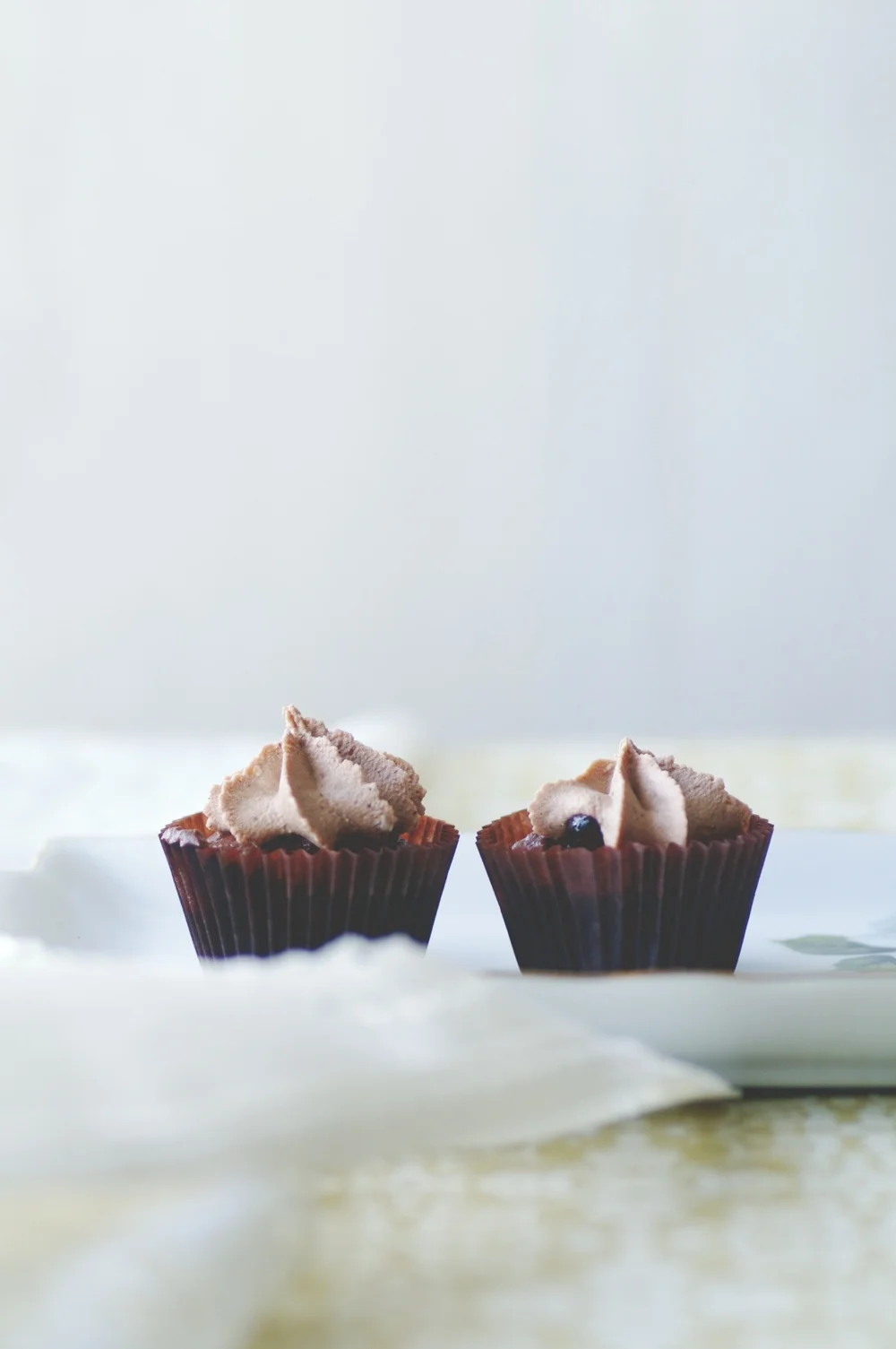 Two small dessert cups with swirled cream and berries on a white plate, soft neutral mood
