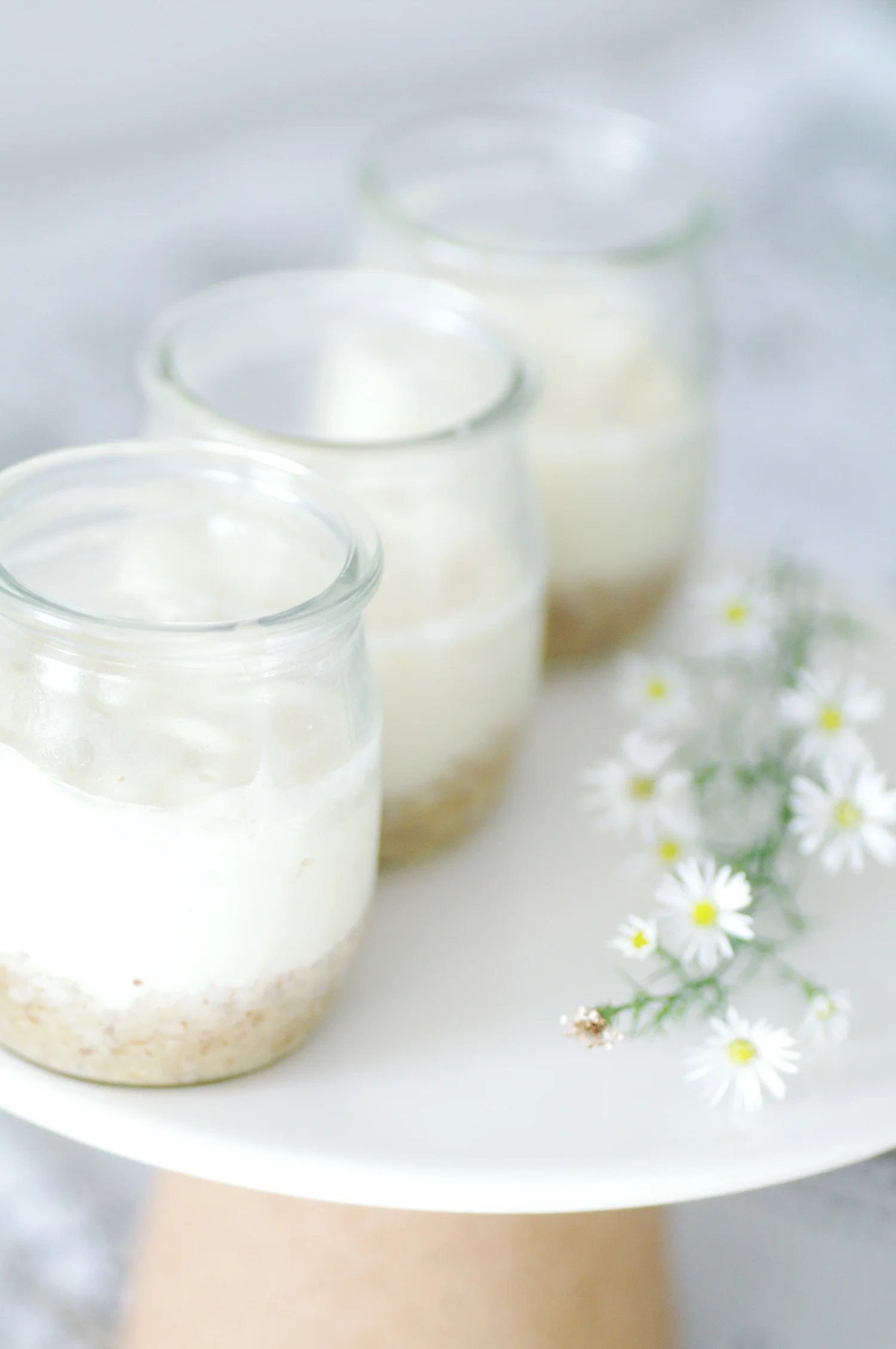 Layered dessert jars with crumb base and small white daisies on a light surface, calm and simple mood