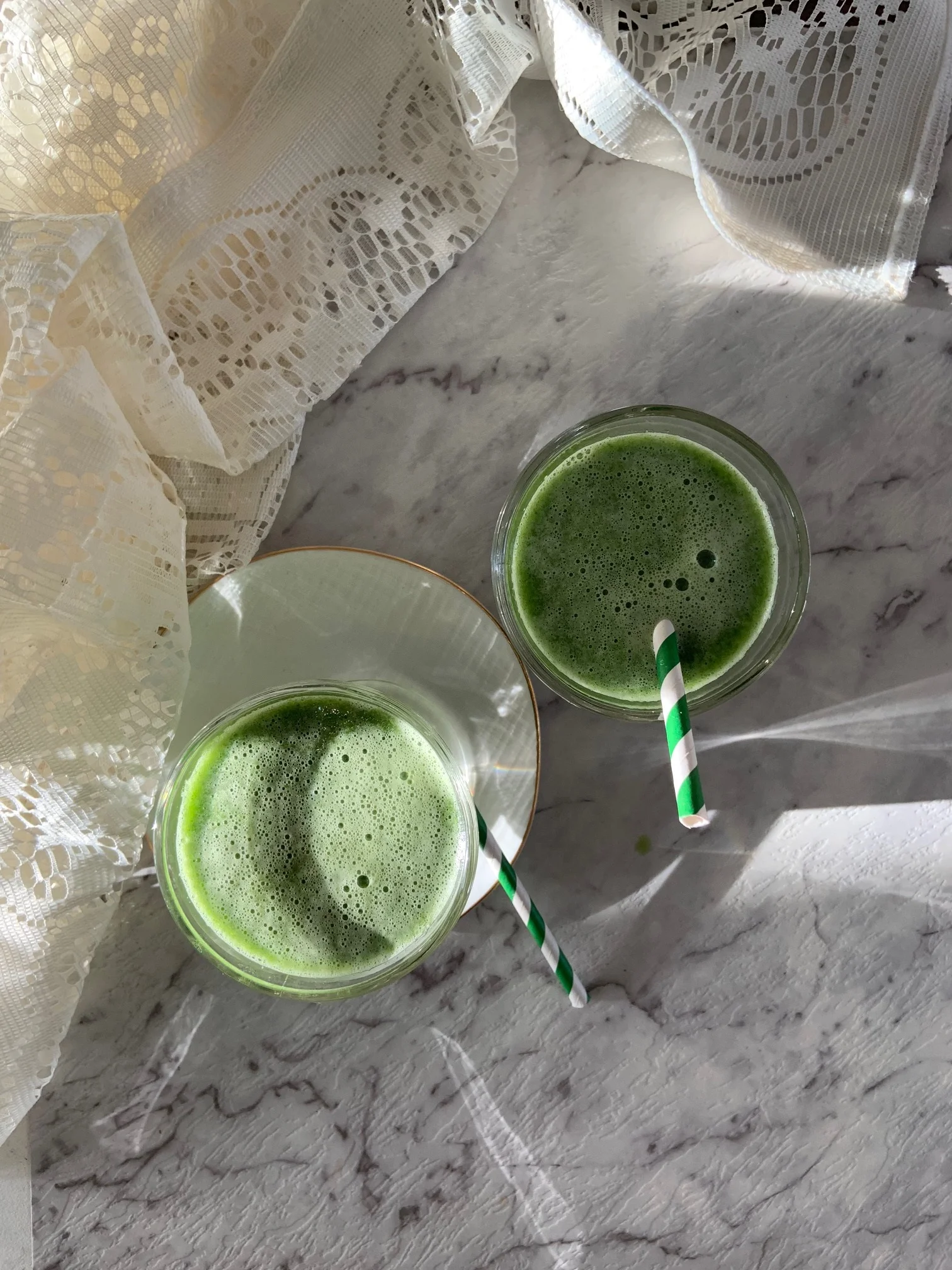 Two green smoothies in glasses with striped straws on a marble surface, a relaxed and casual mood